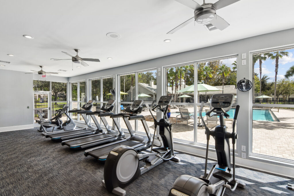 a gym with cardio equipment and windows overlooking a pool
