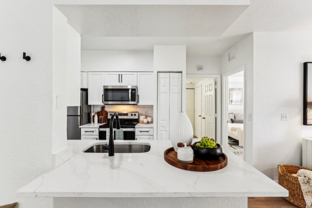 Kitchen with island sink, appliances, wood-style flooring, and designer lighting