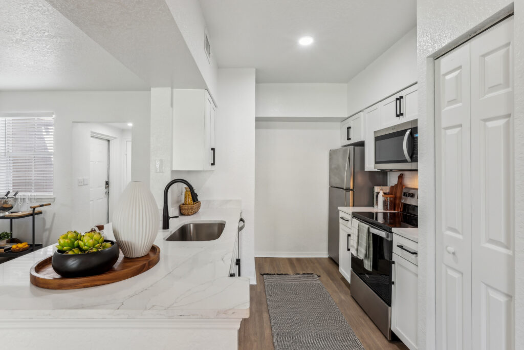 Kitchen with island sink, appliances, wood-style flooring, and designer lighting