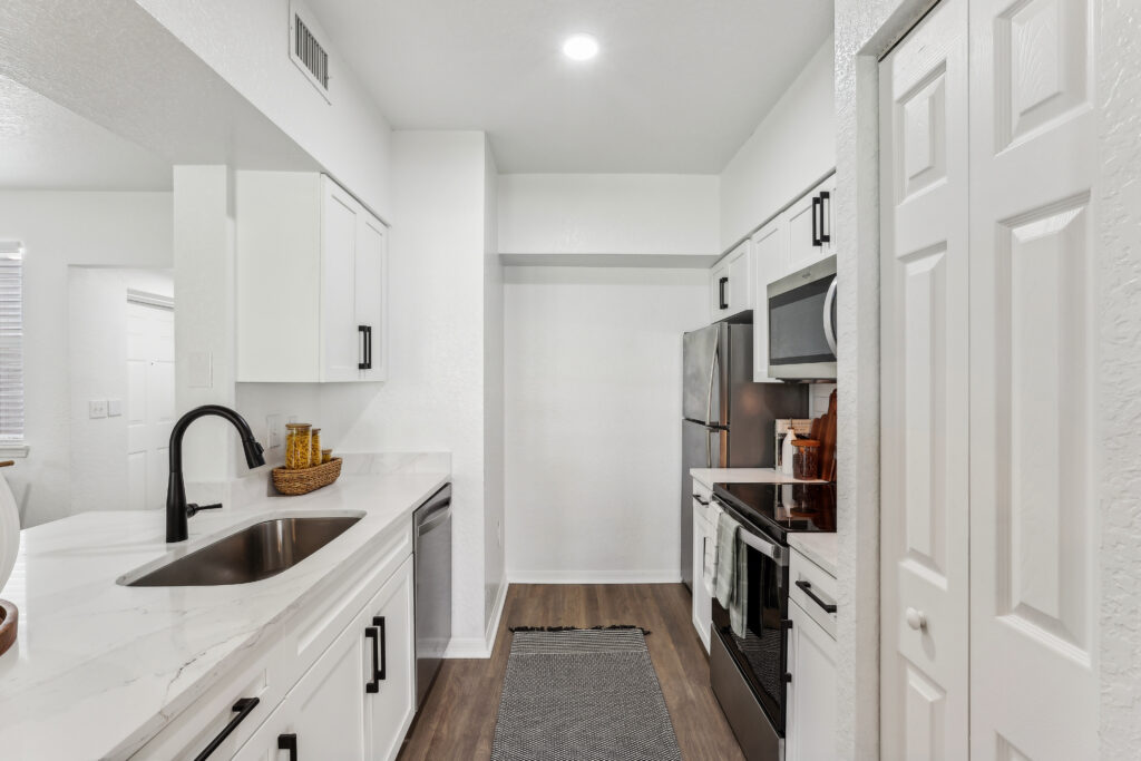 Kitchen with island sink, appliances, wood-style flooring, and designer lighting