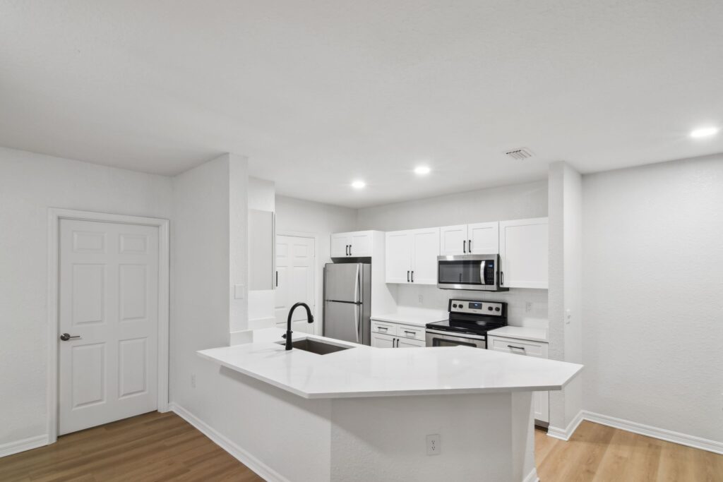 Kitchen with access to the living room, island sink, appliances, wood-style flooring, and designer lighting