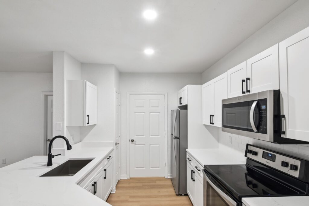 Kitchen with island sink, appliances, wood-style flooring, and designer lighting