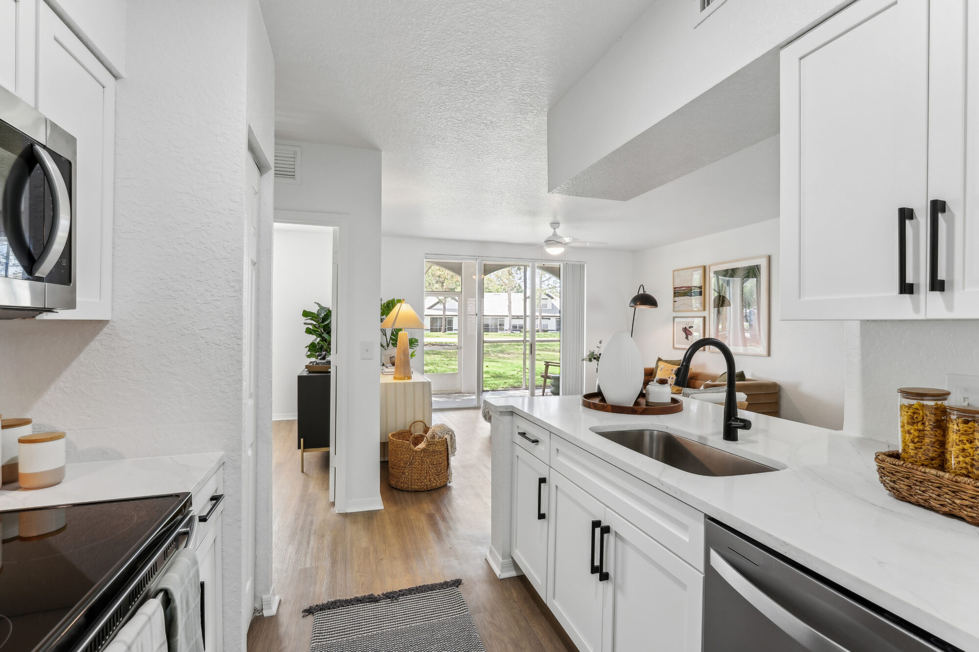Kitchen with island sink, appliances, wood-style flooring, designer lighting, and open access to living room