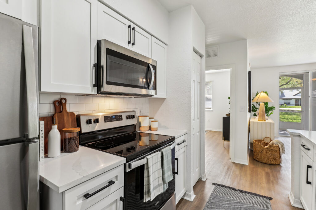 Kitchen with appliances, wood-style flooring, designer lighting, and open access to living room